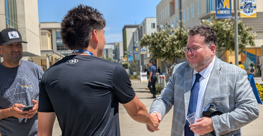 Student shakes hand of UC Merced Dean of Students Jose Leon on a sunny day on campus