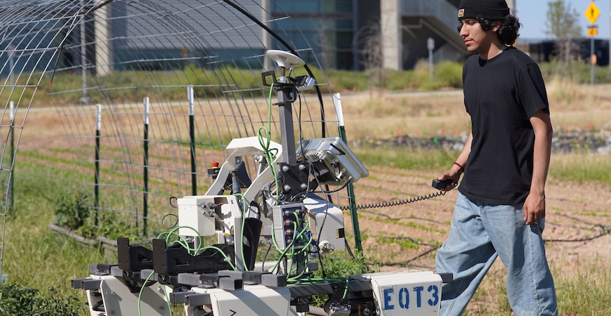 Photo depicts UC Merced student Jesse Martinez operating a robot on the Experimental Smart Farm.