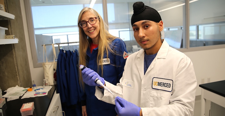 Professor Patti LiWang and student Adesh Johal, holding a syringe and a test tube, stand in a lab at UC Merced.